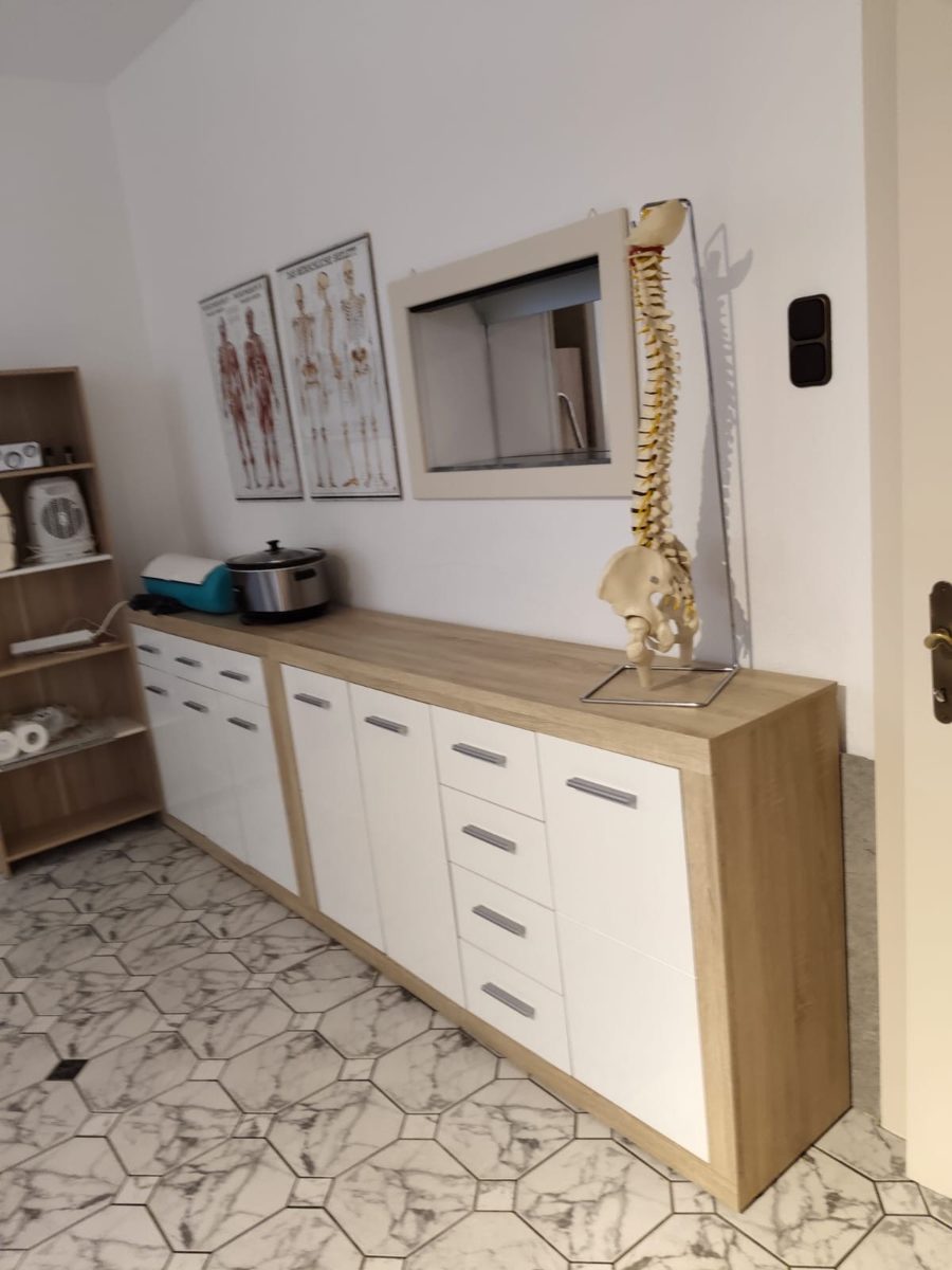 Behandlungsraum mit Anatomie-Postern und Wärmegerät
